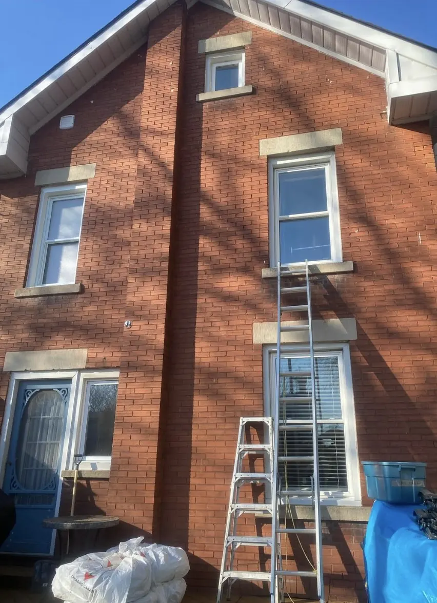Professional window cleaning on two-storey red brick home with ladder in Guelph Ontario